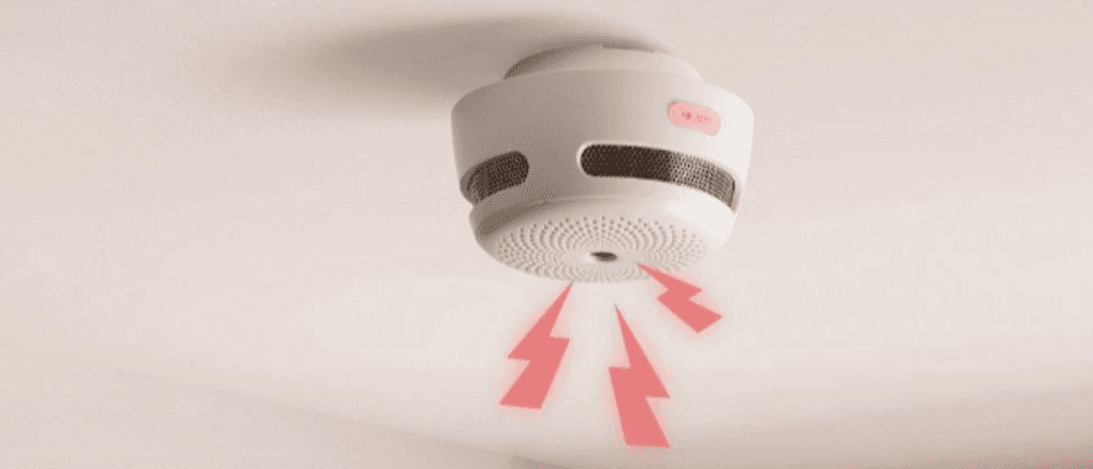 Ein Rauchmelder hängt an der Decke und meldet einen Alarm, was durch Blitze symbolisiert wird.