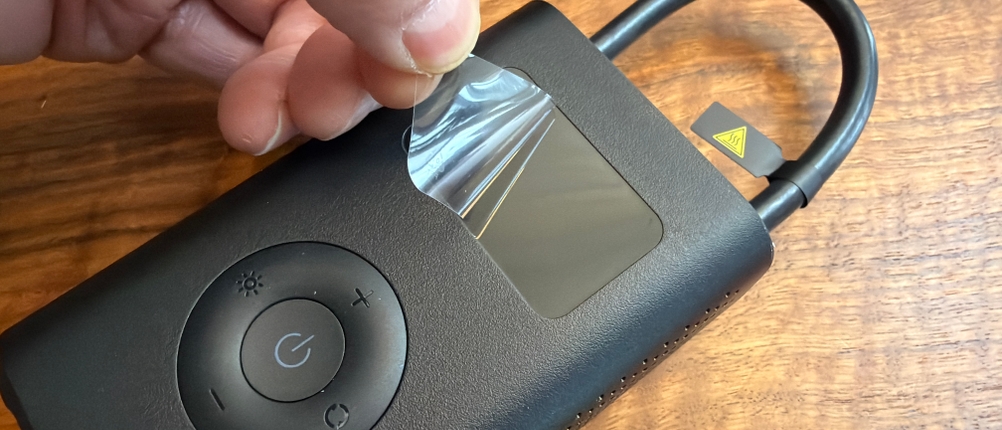 Eine Hand zieht eine Folie vom Display vom Xiaomi Portable Electric Air Compressor 2 ab