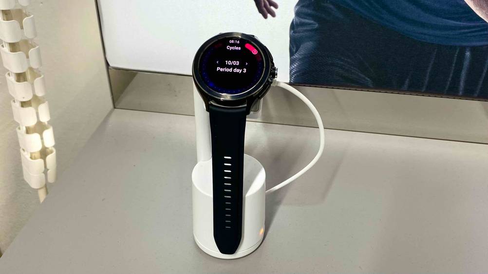 Im Test: Eine Xiaomi-Smartwatch von vorne auf einem weißen Ständer vor einem Plakat.