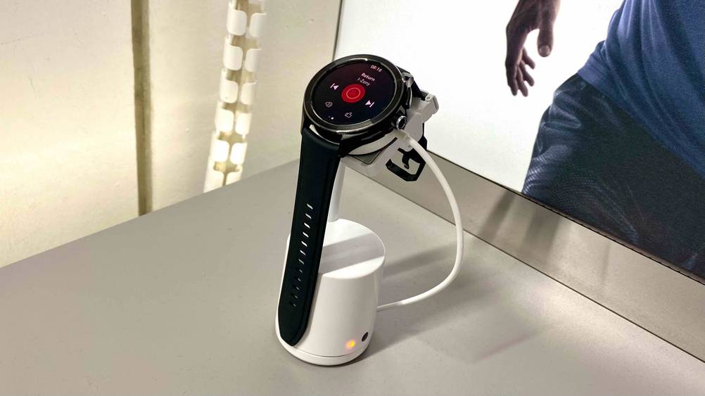 Xiaomi-Smartwatch getestet: Eine Uhr auf einem Ständer von schräg seitlich vor einem Plakat.