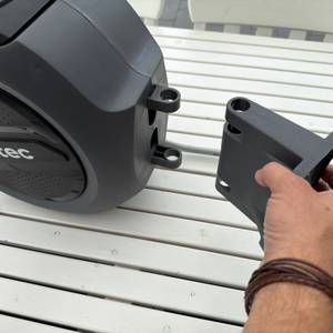 Eine Hand hält die Wandhalterung neben die Xpotool-Schlauchtrommel