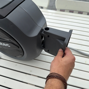 Eine Hand hält die Wandhalterung an die Xpotool-Schlauchtrommel