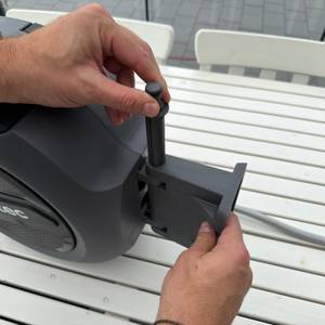 Eine Hand steckt eine Halterung für den Schlauch in die Xpotool-Schlauchtrommel