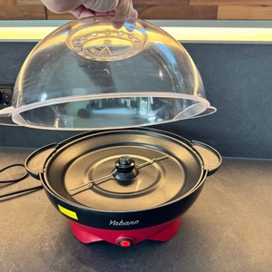 Eine Hand hebt den Deckel der Yabano-Popcornmaschine ab
