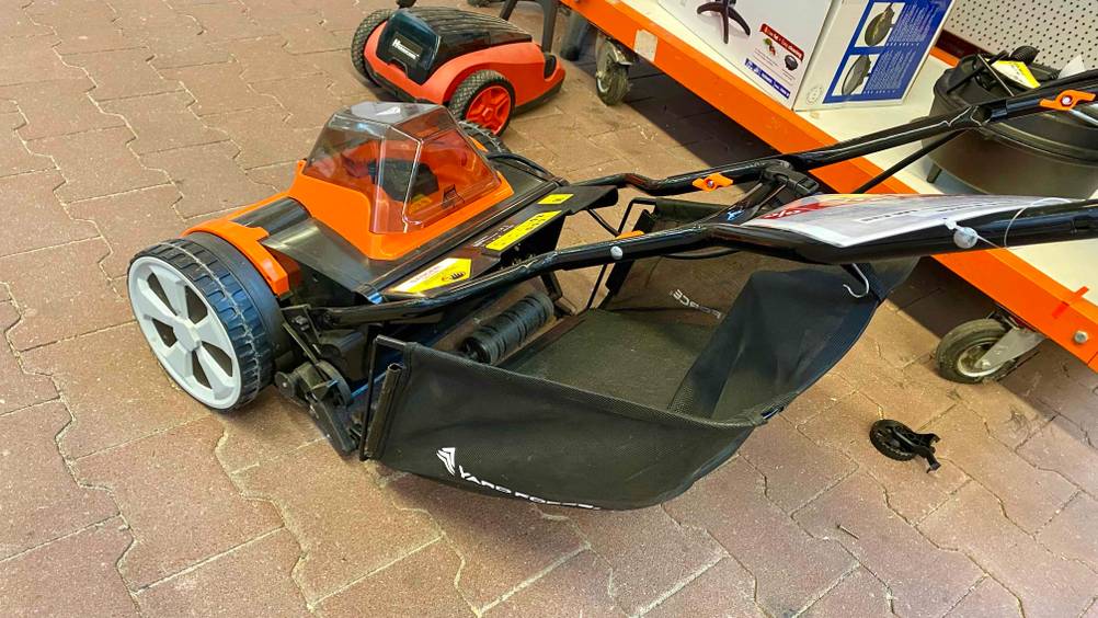 Im Test: Ein Spindelmäher von schräg hinten mit Fokus auf das Netz vor einem Verkaufsregal im Baumarkt.