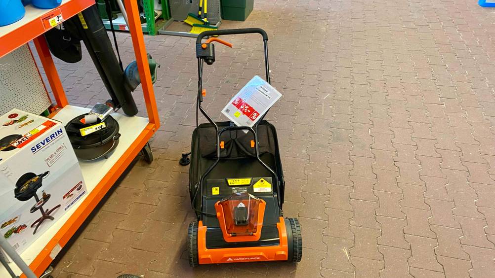 Ein getesteter Spindelmäher von vorne auf einem Steinpflaster in einem Baumarkt.