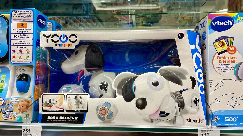 Im Test: ein Roboterhund von Yoco n'friends in weiß-schwarzer Aufmachung steht in seinem Karton mit Sichtfenster auf einem Verkaufsregal zwischen weiteren Robooter-Spielen.