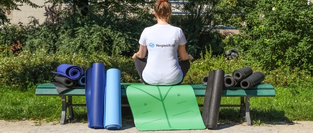 Eine Frau sitzt auf einer Bank mit dem Rücken zur Kamera, auf und an der Bank zahlreiche Yogamatten.