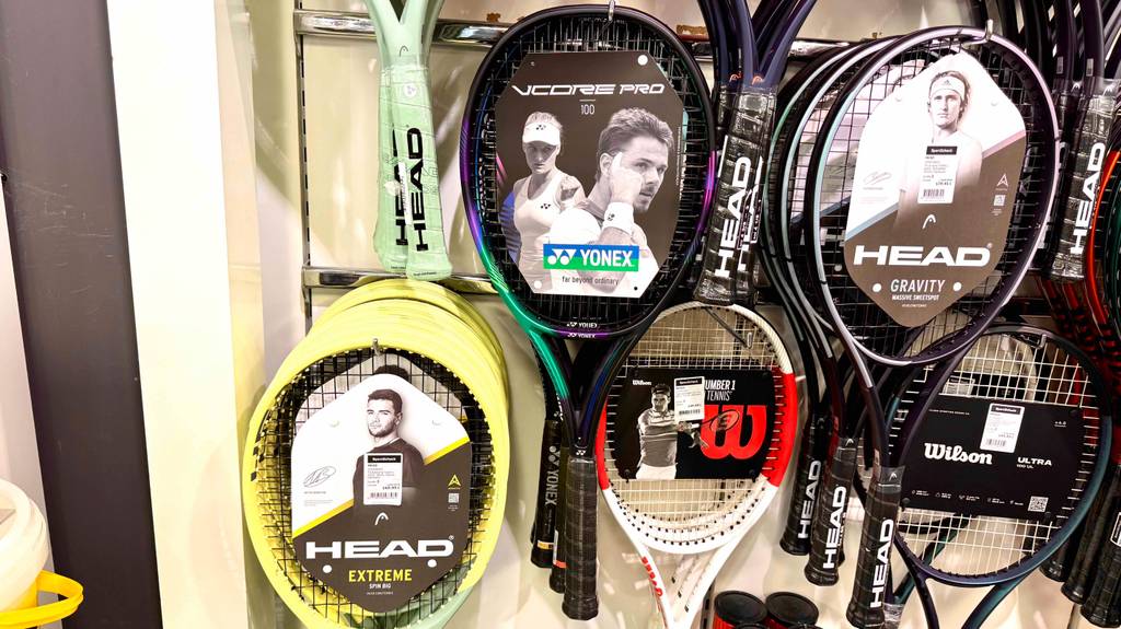 Yonex-Tennisschläger im Test: Mehrere Schläger hängen zwischen Schlägern anderer Marken an einem Wandregal.
