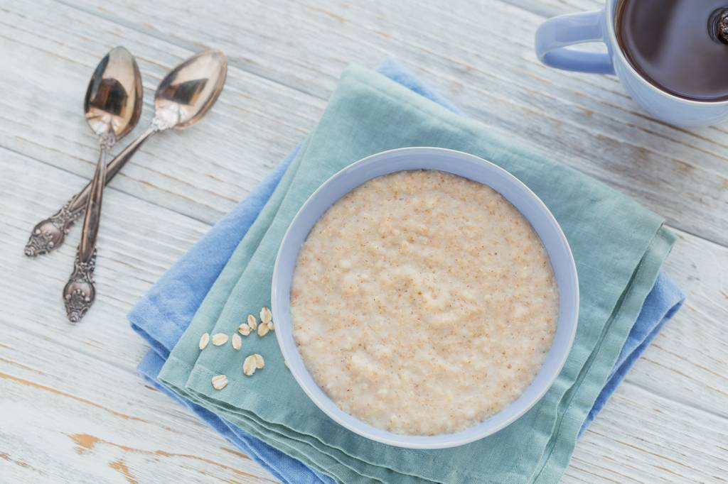 Yum-Asia-Reiskocher-Test: Auf einem Tisch steht ein Schälchen mit Porridge auf einer blauen Serviette. Daneben befinden sich zwei Löffel aus Silber und eine Tasse Tee. 