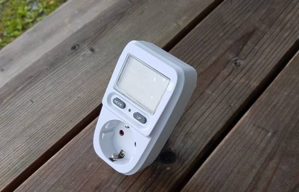 Energiemessgerät im Test: weißes Modell von Zaeel liegt auf einem Holztisch im Außenbereich.
