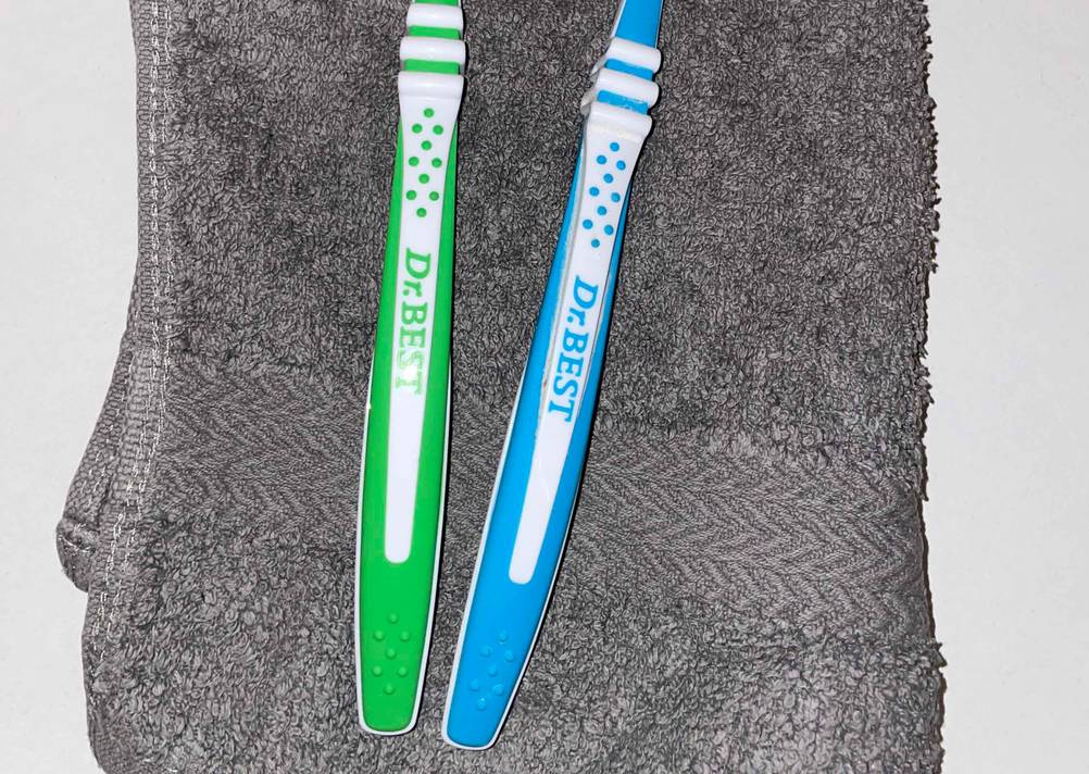 Zahnbürsten im Test: Nahaufnahme der Griffe mit Logo auf einem grauen Handtuch.