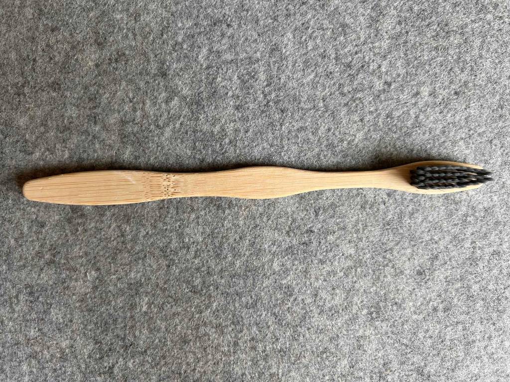 Bambus-Zahnbürste getestet: Eine Zahnbürste von oben mit schwarzen Borsten auf einer grauen Fläche.
