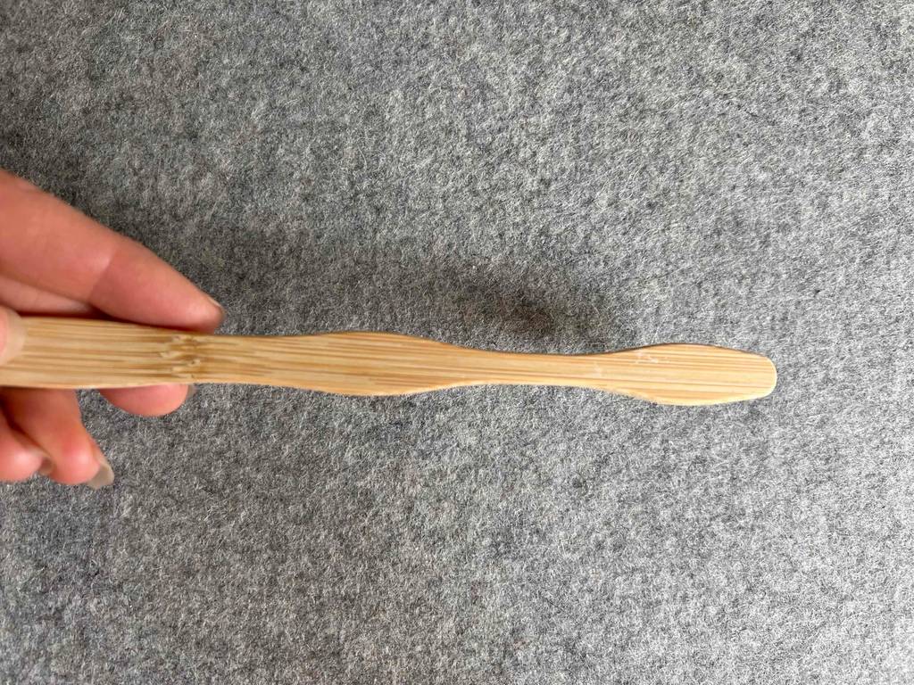 Eine Hand hält die Rückseite einer Bambus-Zahnbürste über eine graue Filzfläche.