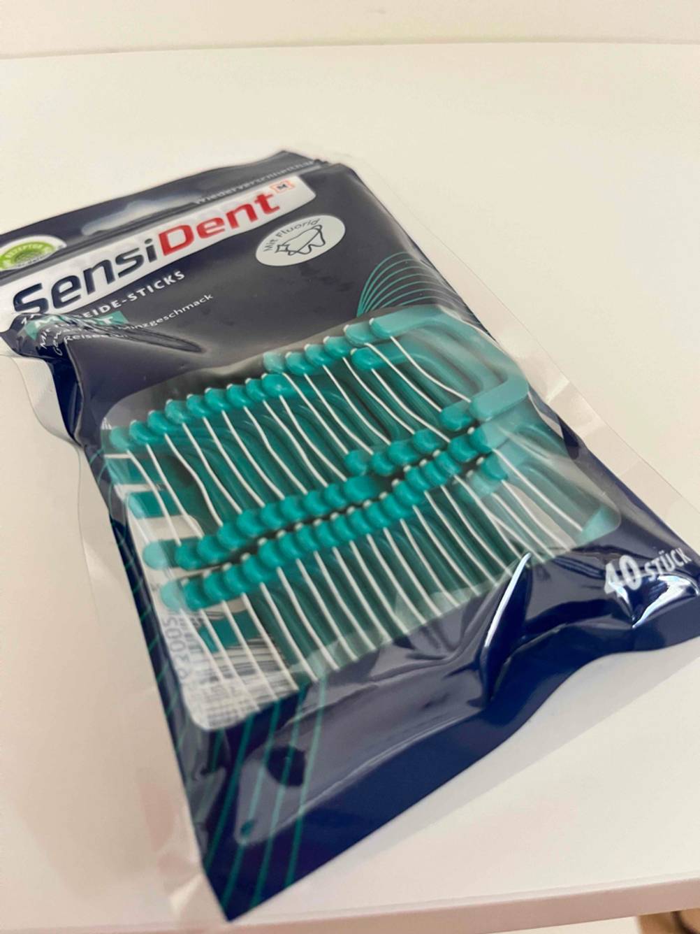 Eine Packung der getesteten Zahnseidenhalter mit transparentem Fenster auf einer hellen Fläche.