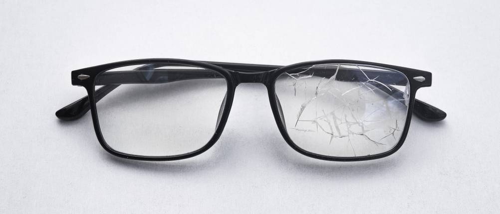 Zahnzusatzversicherungen im Vergleich: Eine Brille mit einem gebrochenen Brillenglas liegt auf einem grauen Untergrund.