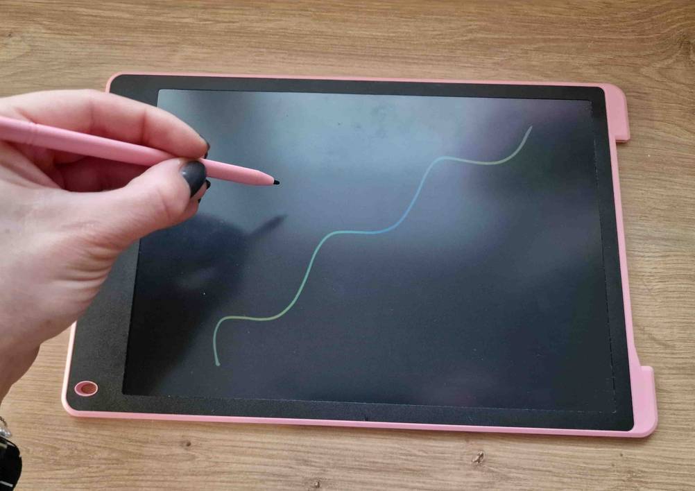 Hand malt mit dem optischen Stift eine Kurvenlinie auf den Bildschirm einer rosa getesteten Zaubertafel.