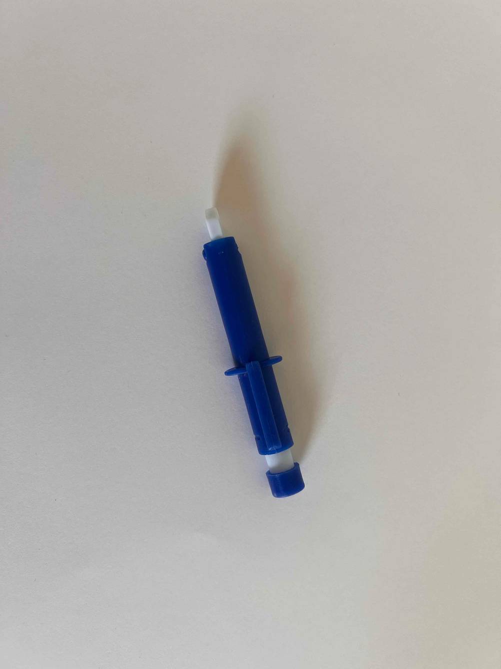 Eine seitlich liegende Zeckenzange im Test von oben auf einer hellen Fläche.