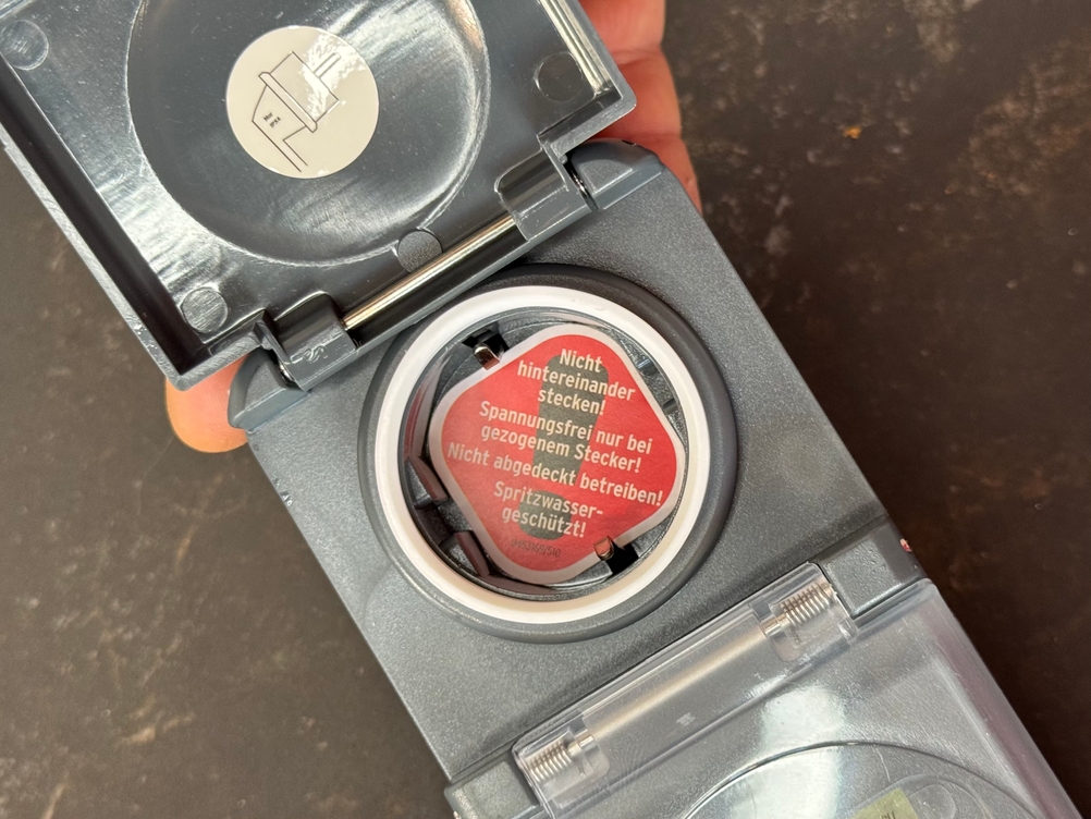 Eine Person öffnet die Klappe der Steckdose bei der getesteten Zeitschaltuhr von Brennenstuhl.
