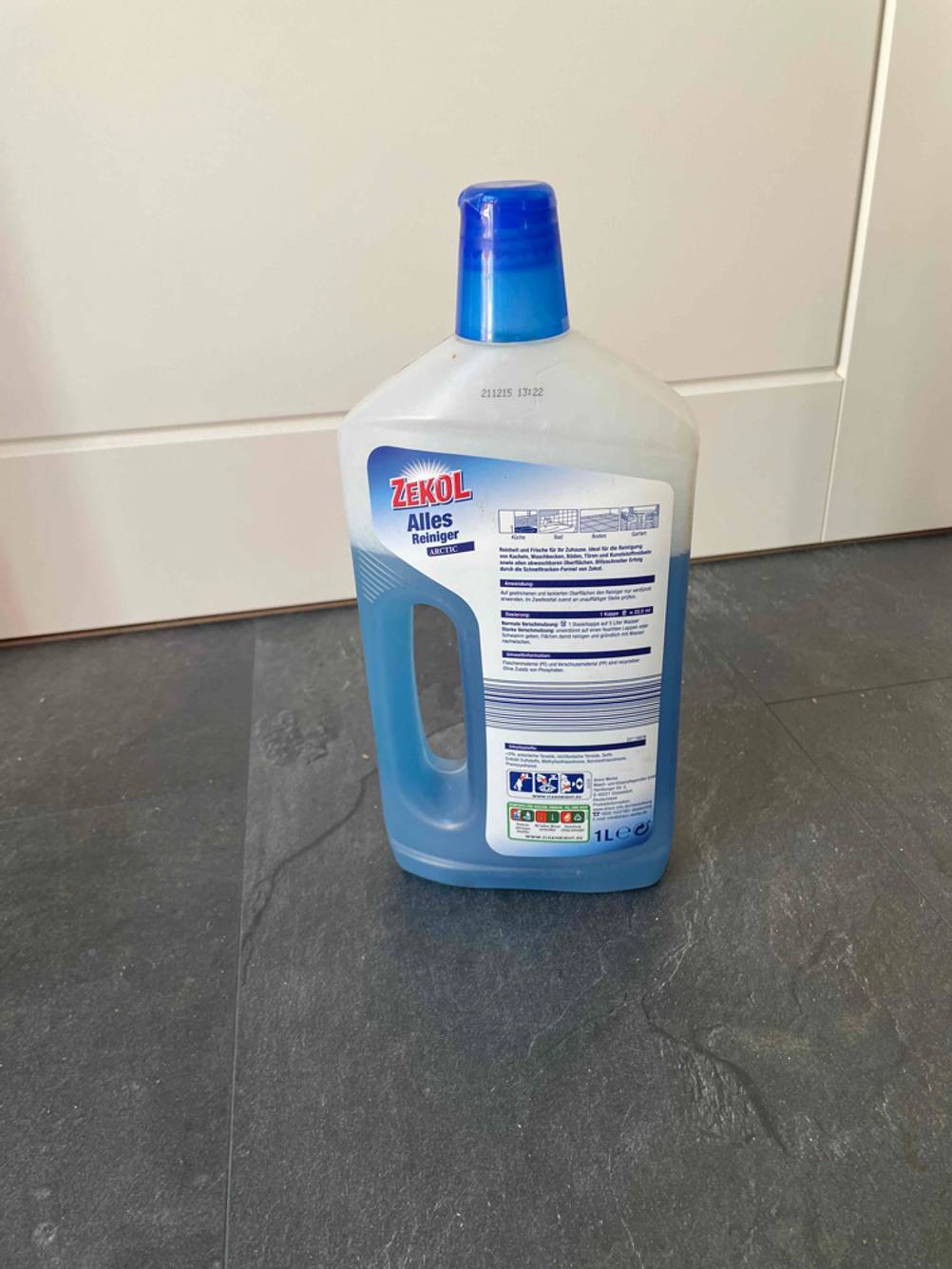 Im Test: Rückseite einer Flasche Allzweckreinigers vor einer hellen Wand auf einem Steinboden stehend.