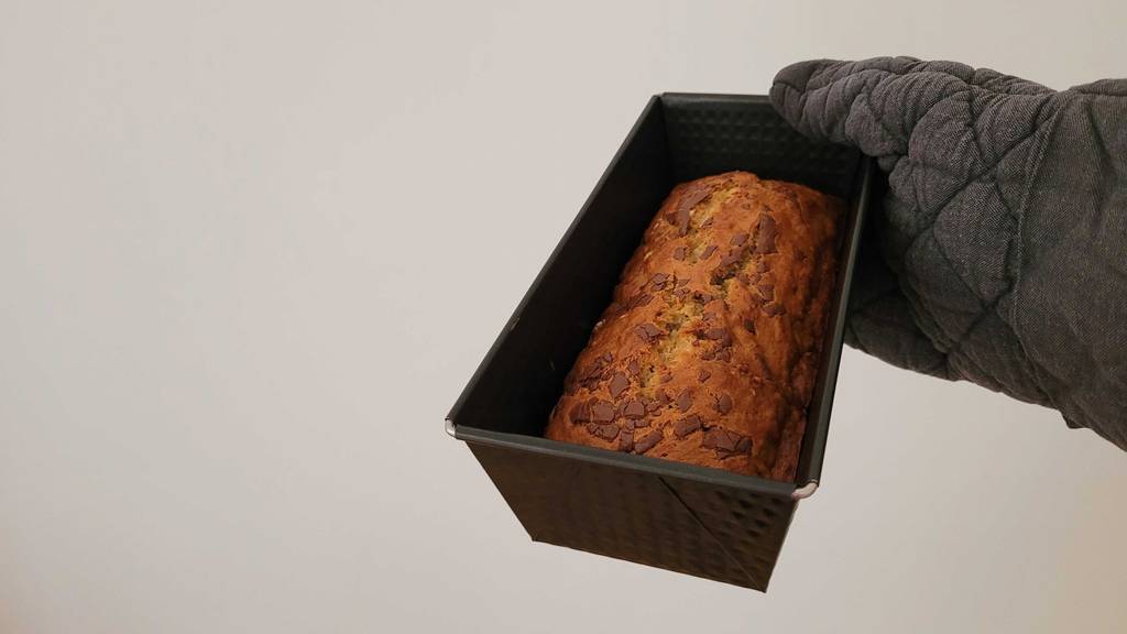 Eine getestete Backform inklusive gebackenem Kuchen von einer Hand mit hitzebeständigem Ofenhandschuh gehalten.