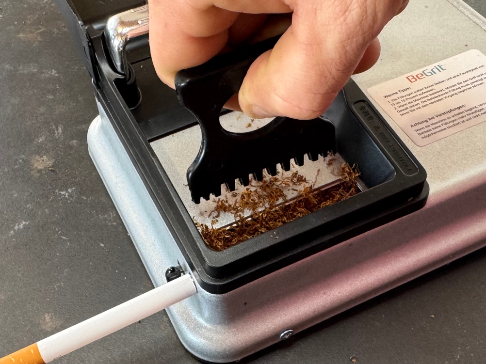 Eine Person schiebt Tabak mit einem kleinen Kamm in die getestete Zigarettenstopfmaschine von BeGrit.