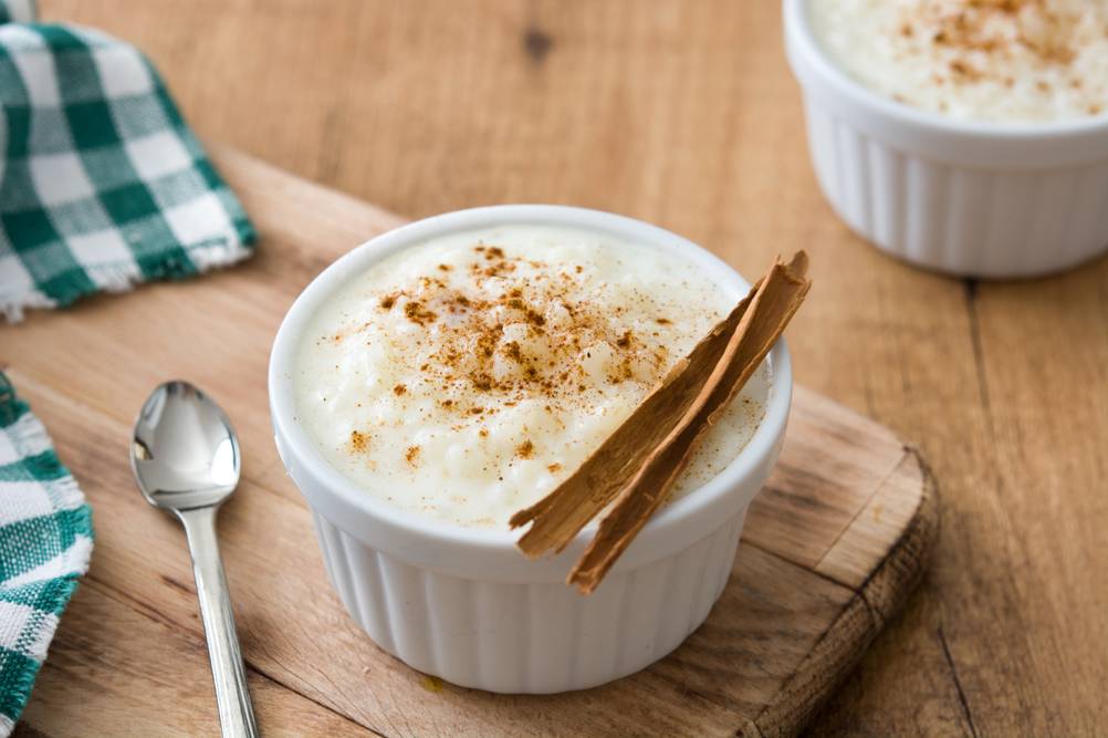 Zimtstangen-Test: Auf einem Holzbrett steht eine Schale mit Milchreis. Der Milchreis ist mit Zimtstangen und gemahlenem Zimt garniert. 