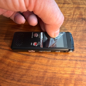 Eine Hand zieht eine Folie vom Display des Zipcide-Diktiergerät ab