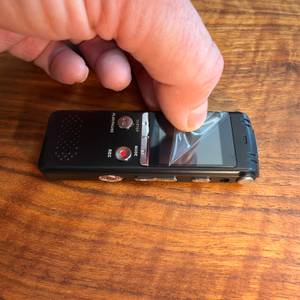 Eine Hand zieht eine Folie vom Display des Zipcide-Diktiergerät ab