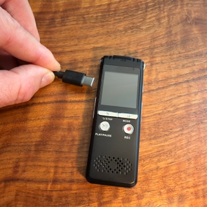 Eine Hand steckt ein Ladekabel in das Zipcide-Diktiergerät