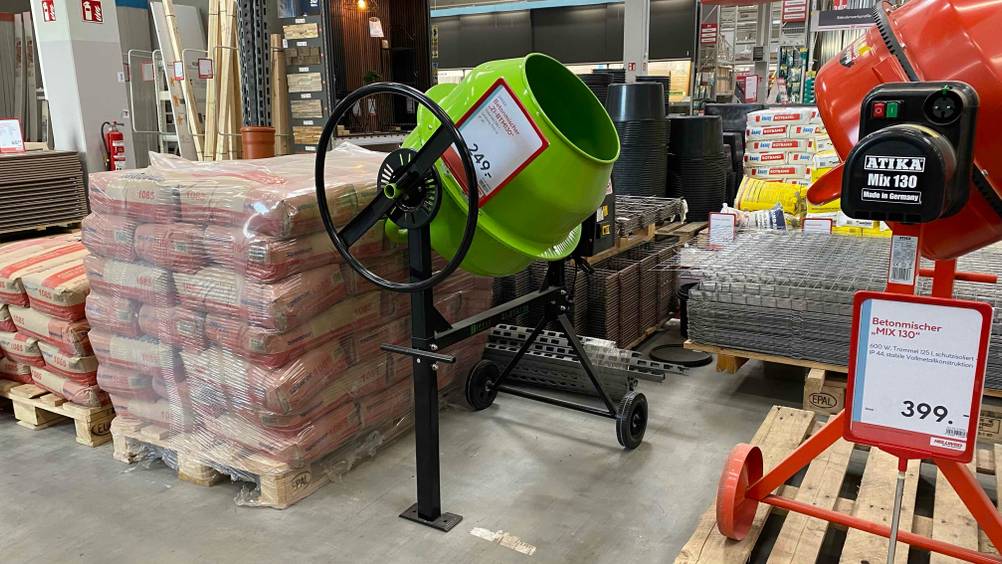 Betonmischer getestet: Ein grüner Betonmischer steht zwischen anderen Produkten mit einem Preisschild in einer Verkaufsfläche.
