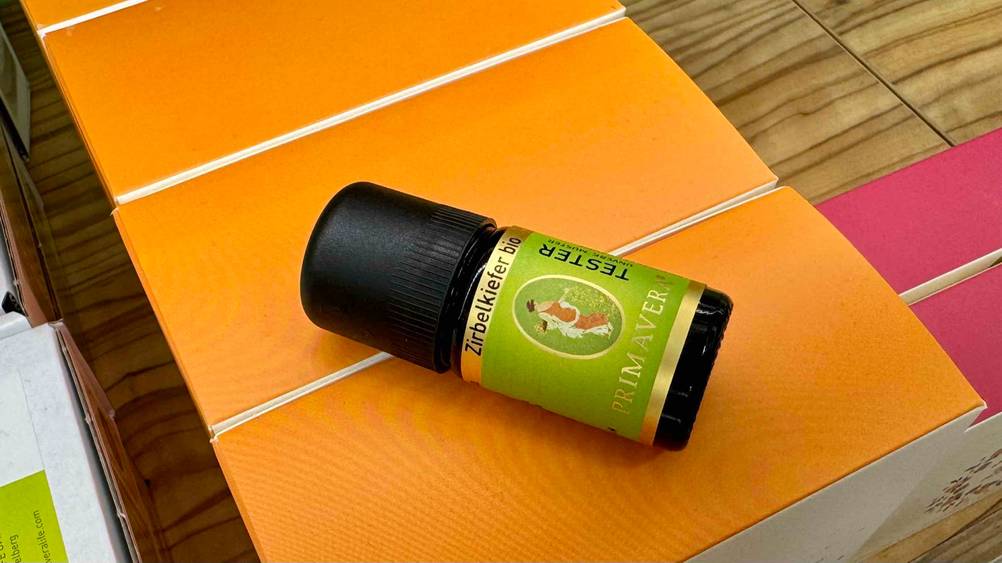 Ein Fläschchen des getesteten Zirbenöls liegt auf einem orangenem Karton.