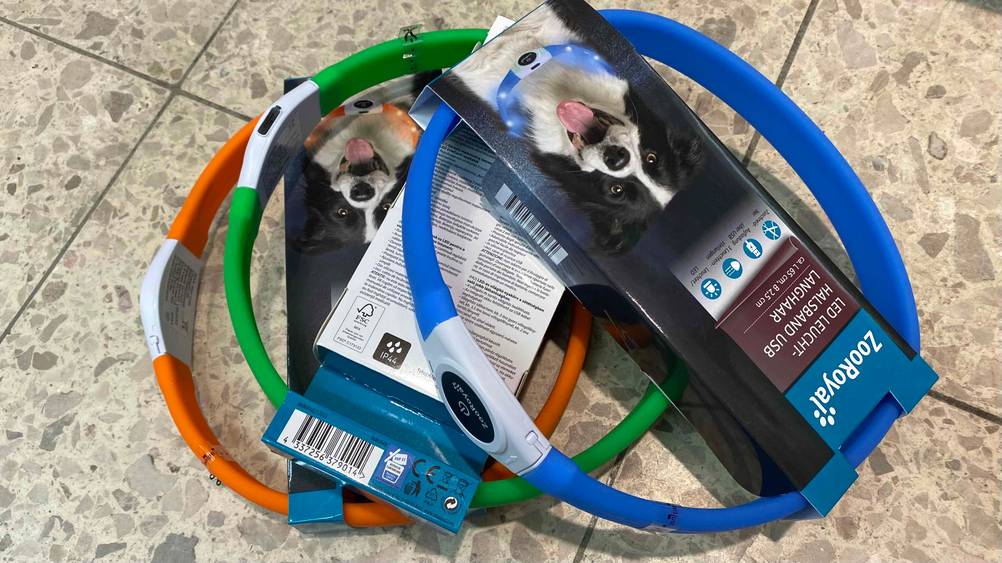 Mehrere verschiedenfarbige Leuchthalsbänder für Hunde im Test auf einem Fliesenboden.