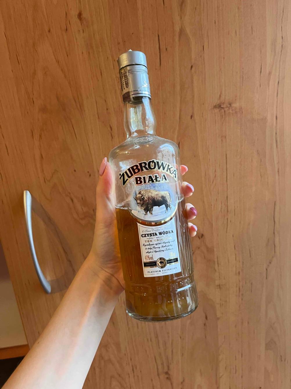 Eine Hand hält eine Flasche getesteten polnischen Wodka vor einer Schranktür.