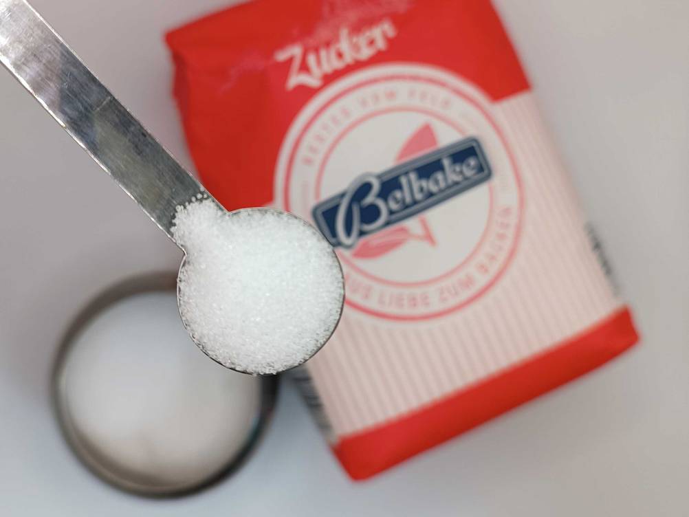 Zucker getestet: Nahaufnahme eines Löffels mit Zucker, im Hintergrund die Originalverapckung.