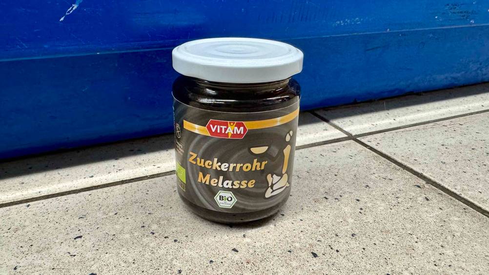 Zuckerrohrmelasse getestet: Ein Glas steht vor einer blauen Wand auf dem Boden.
