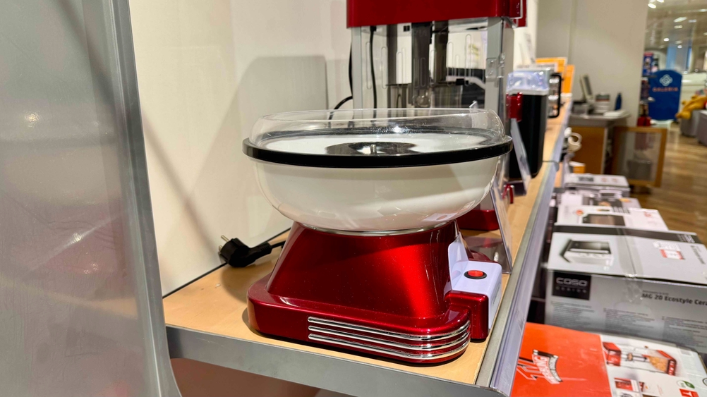 Eine Zuckerwattemaschine im Test von der Seite auf einem Verkaufsregal mit anderen Produkten stehend.