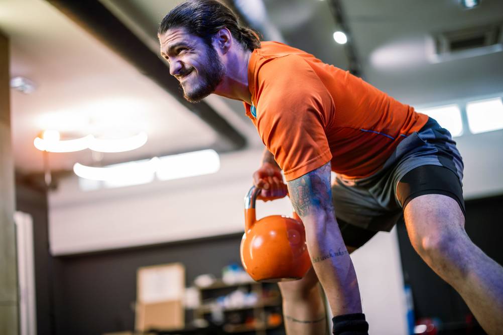 Ein Mann trainiert in halb hockender Position mit einer Kettlebell. Der Gesichtsausdruck ist angestrengt.