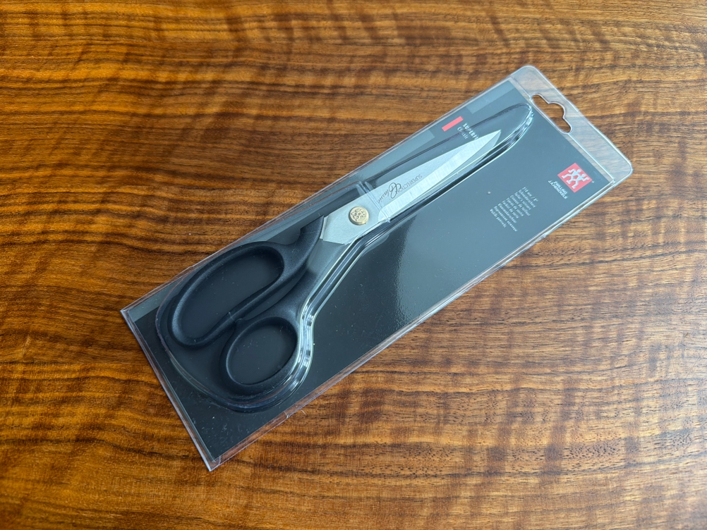 Die Zwilling-Schneiderschere liegt in ihrer Verpackung auf einem Tisch