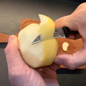 Eine Hand schält mit dem Zwilling-Schälmesser eine Nashi-Birne.