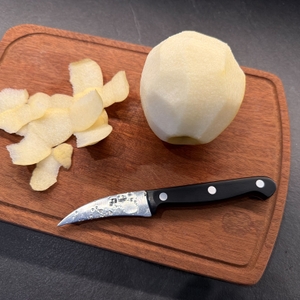 Das Zwilling-Schälmesser liegt neben einer geschälten Nashi-Birne auf einem Brett.