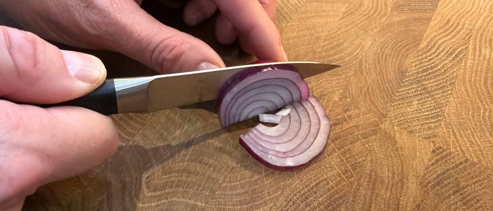 Eine Hand schneidet mit dem Zwilling-Vier-Sterne-Spick- und Garniermesser eine Zwiebel