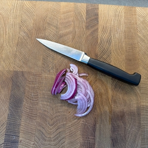 Eine geschnittene Zwiebel liegt neben dem Zwilling-Vier-Sterne-Spick- und Garniermesser