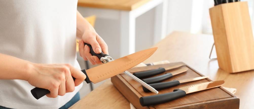 zwilling-wetzstahl-test: Eine Frau steht vor ihrem Messerset und schärft ein Messer nach dem anderen.