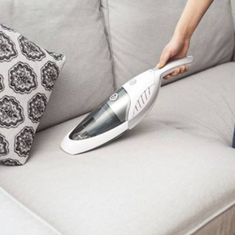 sofa wird mit akku-handstaubsauger gesaugt