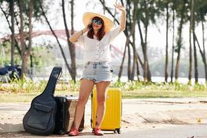 junge frau mit koffern und gitarrentasche am strassenrand