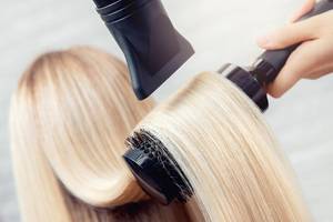frau bekommt ihre langen blonden haare mit einem föhn und einer rundbürste gestylt