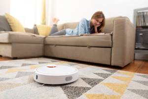 Staubsauger-Roboter im Test: Roboter reinigt den Teppich, während eine Frau auf dem Sofa entspannt.