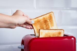 frau nimmt fertig getoastete brotscheiben aus dem toaster
