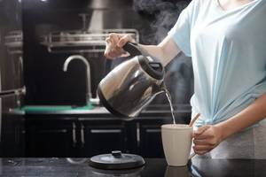 frau fuellt wasser aus dem wasserkocher in eine tasse